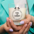 a wood wick candle in a glass jar with the Coal & Canary logo.
