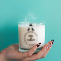 a wood wick candle in a glass jar with the Coal & Canary logo.