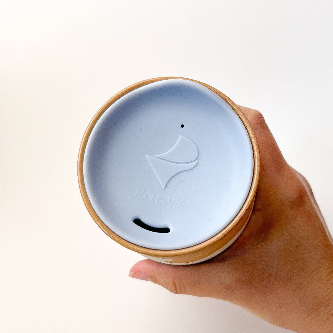 Mountains Travel Mug, a ceramic mug with a matte finish, with a mountain scape around the perimeter. Comes with a blue silicone lid.