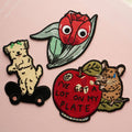 Set of four colorful patches featuring a dog, a pea pod, an apple with text, and a mouse on a pink background.