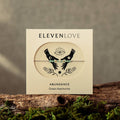 Product packaging for 'Eleven Love' with hands and eye design on a wooden surface with moss.