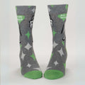 A pair of men's crew socks with a grey background and a pattern of white starbursts and green accents. One sock features the rear end of a white donkey and the text "ALL PUNS INTENDED," while the other shows the front half of the donkey.
