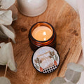 Candle in a decorative container on a wooden surface with eucalyptus leaves.