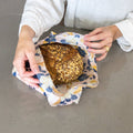 Person holding a loaf of bread wrapped in a reusable fabric food wrap on a neutral background