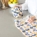 Person using floral-patterned food wraps on a kitchen counter with lemons in the background.