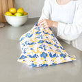 Person holding a floral-patterned cloth bag on a kitchen counter with lemons in the background.