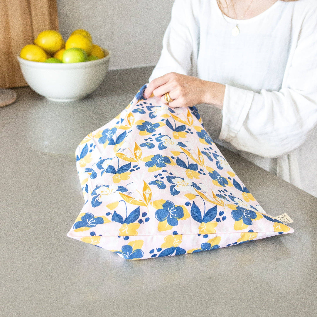 Person holding a floral-patterned cloth bag on a kitchen counter with lemons in the background.