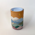 Mountains Travel Mug, a ceramic mug with a matte finish, with a mountain scape around the perimeter. Comes with a blue silicone lid.