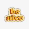 A retro-style sticker with the words "be nice" in a stacked, three-dimensional font with orange and yellow layers, outlined in black, on a light cream background.