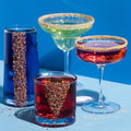 Four cocktail glasses with colorful drinks on a blue background