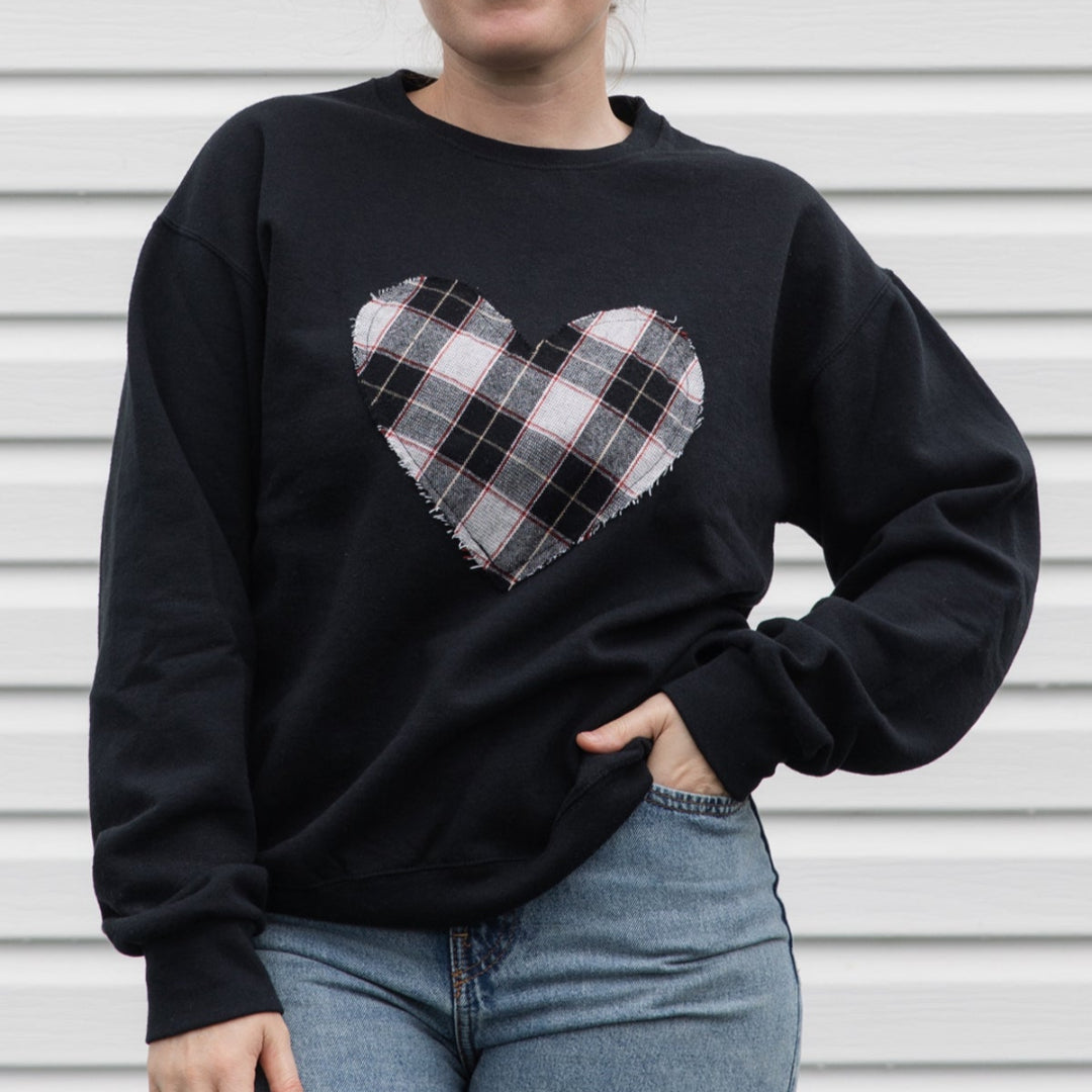 Person wearing a black sweatshirt with a plaid heart design against a metallic background