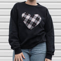 Person wearing a black sweatshirt with a plaid heart design against a metallic background