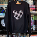 Black sweatshirt with a plaid heart design on a hanger against a bookshelf background