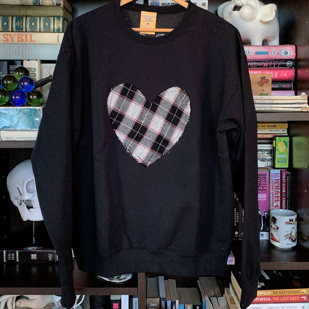 Black sweatshirt with a plaid heart design on a hanger against a bookshelf background