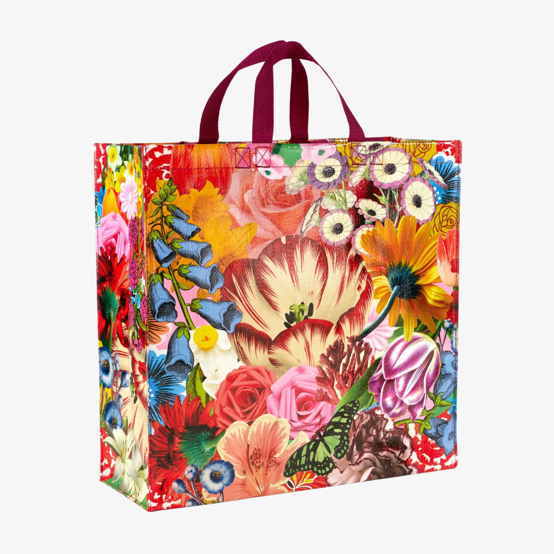 A reusable tote bag with a vibrant floral pattern. The bag features a variety of colorful flowers, including roses, lilies, and tulips, as well as a butterfly. The bag has dark red handles.