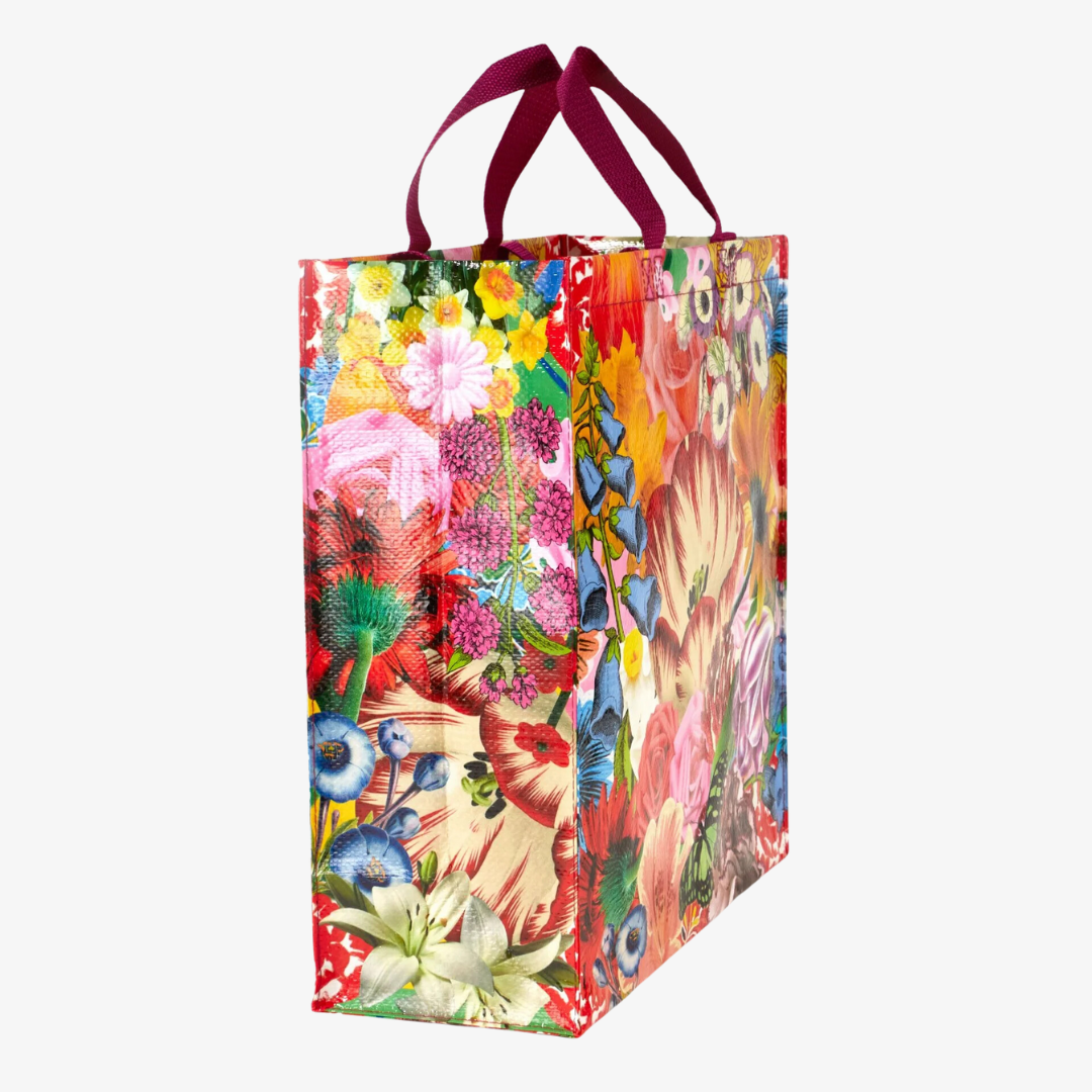 A reusable tote bag with a vibrant floral pattern. The bag features a variety of colorful flowers, including roses, lilies, and tulips, as well as a butterfly. The bag has dark red handles.