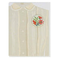 A greeting card featuring an illustration of the top portion of a light-coloured blouse with a Peter Pan collar and vertical stripes. A round button with a floral design in red and green is affixed to the right side of the blouse illustration.