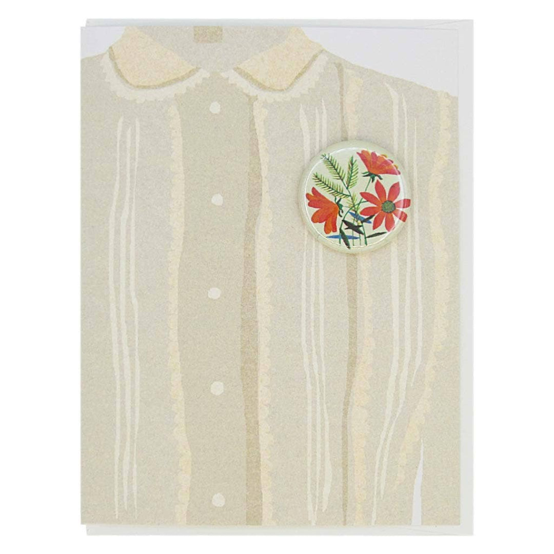 A greeting card featuring an illustration of the top portion of a light-coloured blouse with a Peter Pan collar and vertical stripes. A round button with a floral design in red and green is affixed to the right side of the blouse illustration.