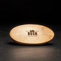 A brown, oval-shaped brush with a wooden handle and natural bristles. The brush is resting on a black surface.