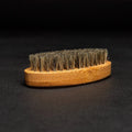 A brown, oval-shaped brush with a wooden handle and natural bristles. The brush is resting on a black surface.