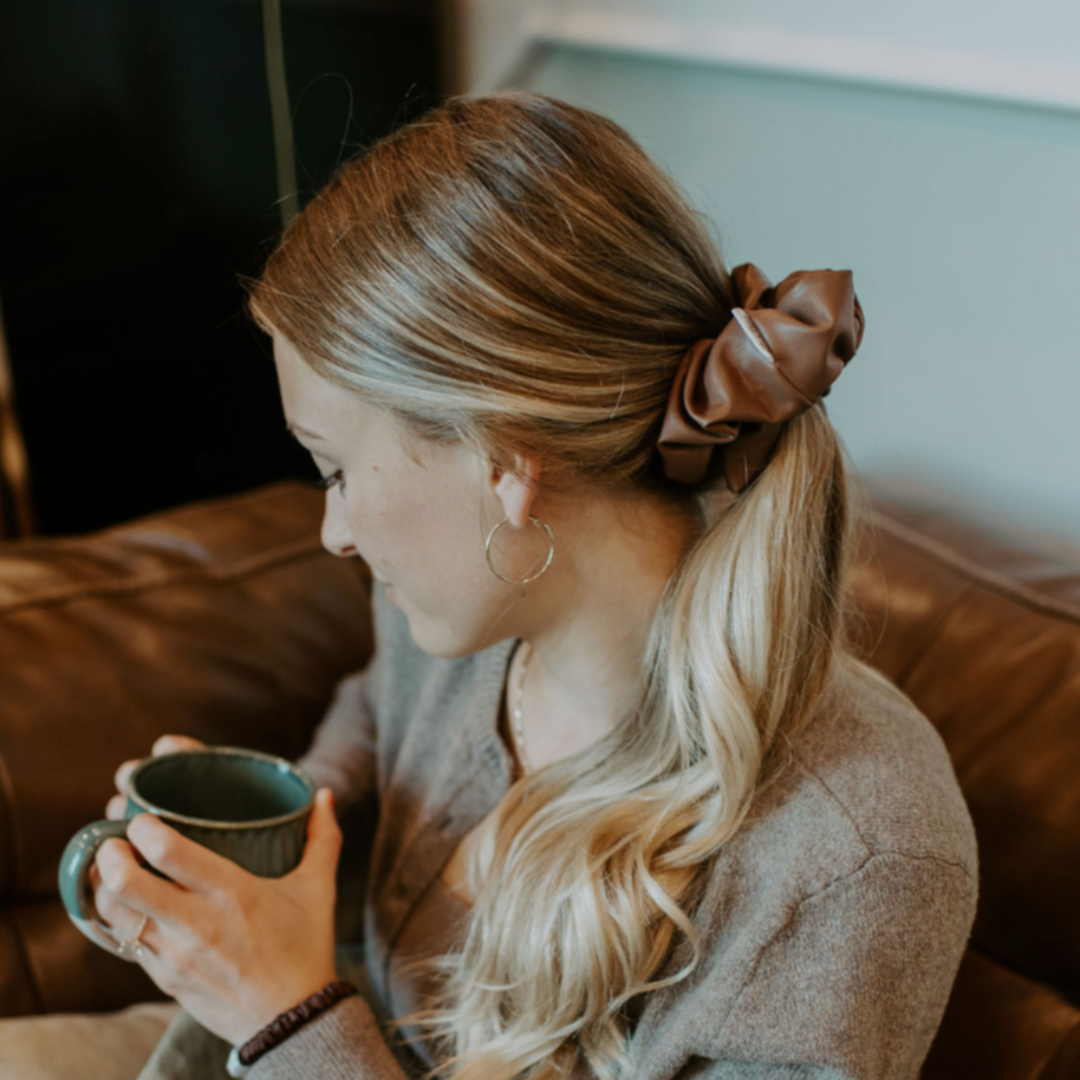 Woman sitting on a couch holding a mug, wrapped in a blanket with a blurred background