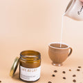 Candle labeled 'Cafe Au Lait' with a cup of coffee and cream being poured, on a beige background.