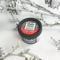 A jar of Candy Cane Mini Natural Deodorant by Undercarriage Deodorant, placed on a white surface surrounded by pine cones and decorated with a red and green label featuring 'Candy Cane'.