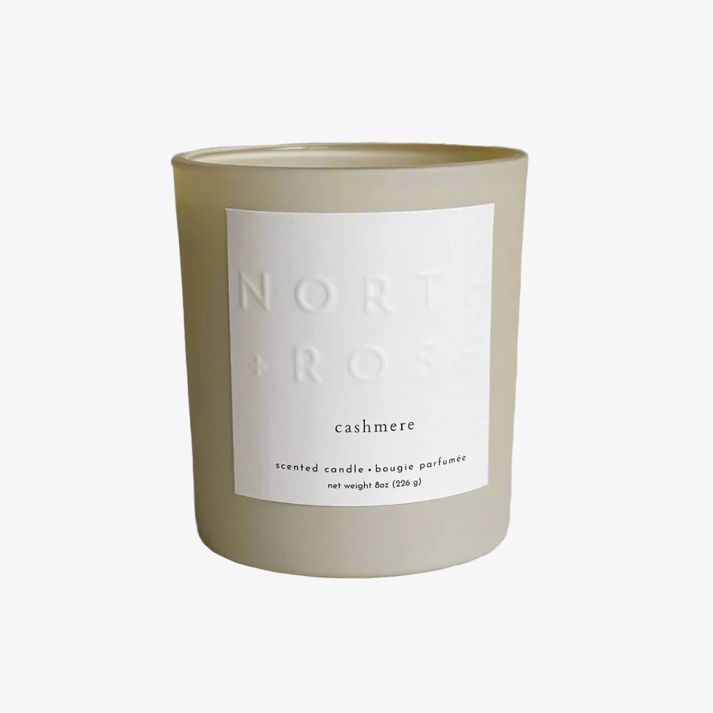 A beige glass jar candle with a white label. The label reads "NORTH ROSE" and "CASHMERE."