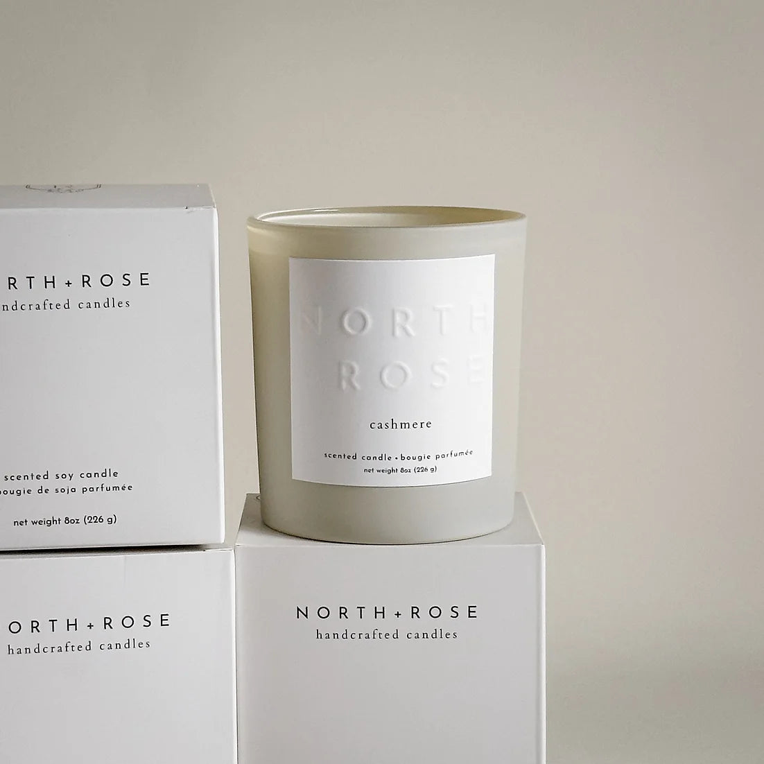 A beige glass jar candle with a white label. The label reads "NORTH ROSE" and "CASHMERE."