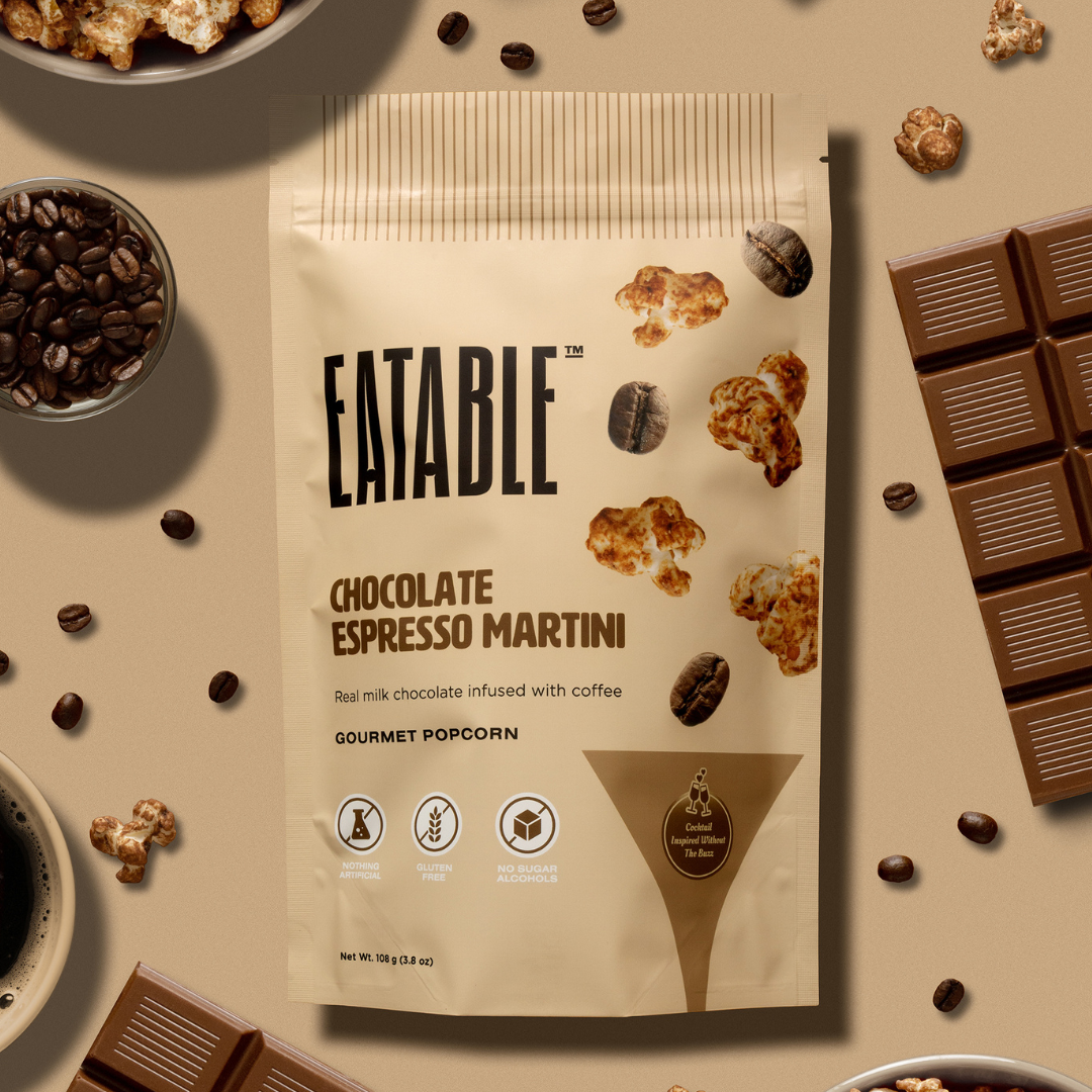Eatable Chocolate Espresso Martini gourmet popcorn package on a table with coffee beans, chocolate, and popcorn.