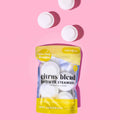 A clear, yellow-accented pouch of "Blazing Bombs" Citrus Blend Shower Steamers is centered on a vibrant pink background. The label specifies the "energize" effect and shows four white, round steamer pucks inside the bag. Three additional white pucks are floating above the bag, casting shadows on the pink surface.