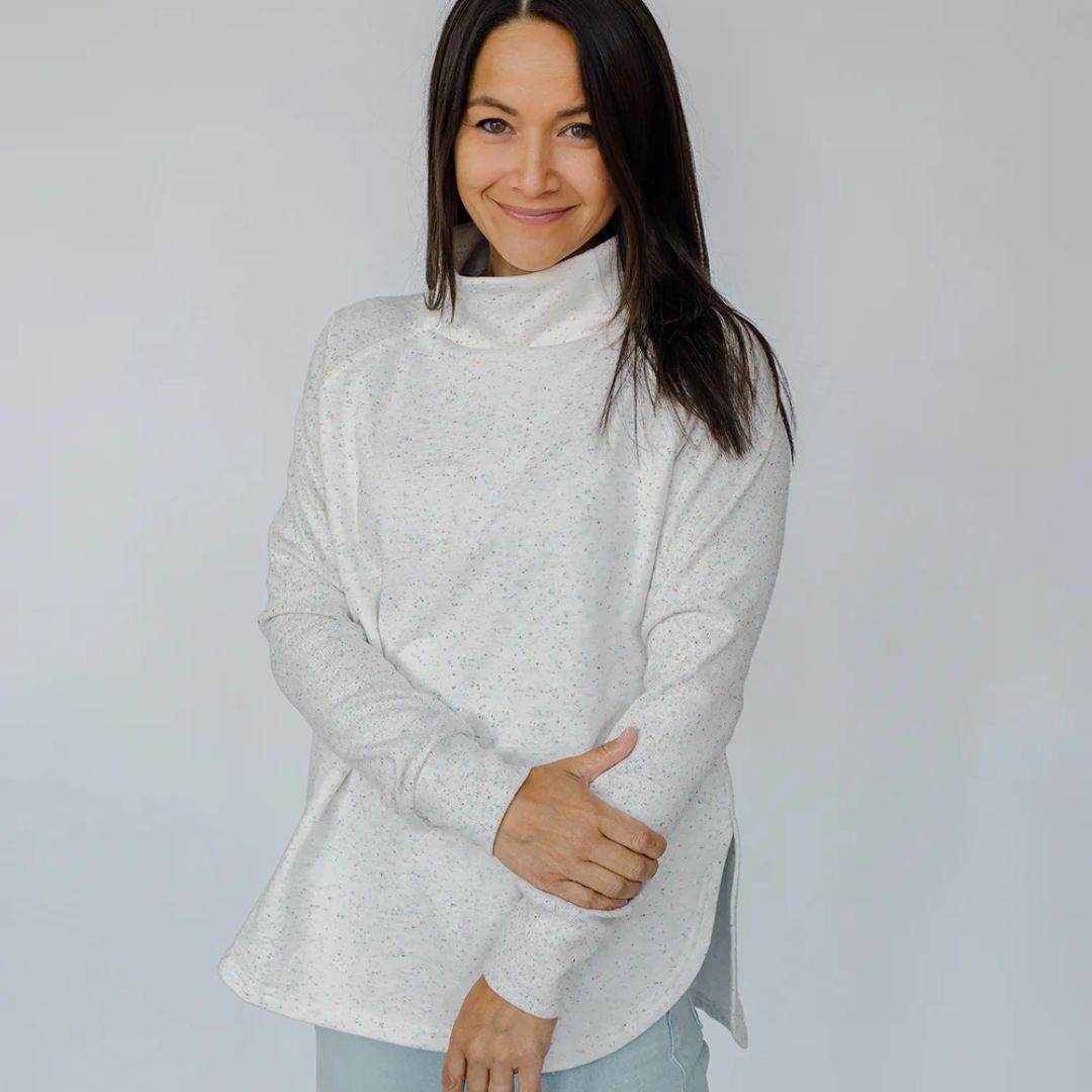 Woman wearing a light gray turtleneck sweater against a plain background