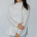 Person wearing a light gray turtleneck sweater against a plain background