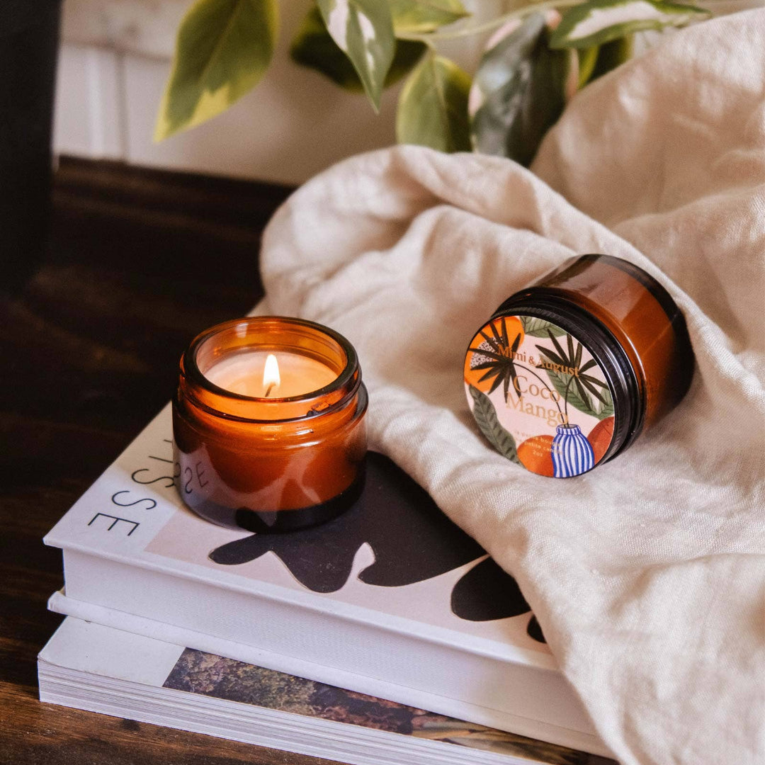 Two amber-colored candles on a stack of magazines with a plant in the background