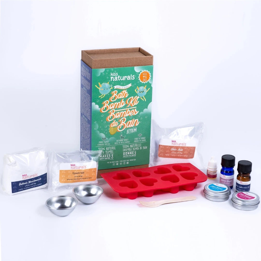 A cardboard box containing a Kiss Naturals Bath Bomb Kit. The box is green and white with the product name and a colorful illustration of bath bombs. It states that the kit is 100% natural, made in Canada, and suitable for ages 6 and up.