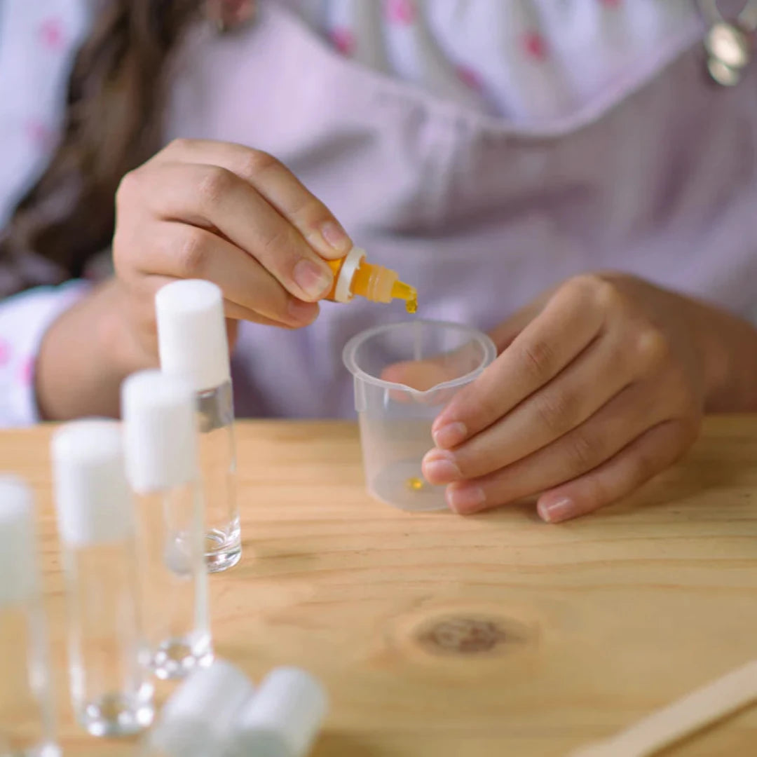 A cardboard box containing a Kiss Naturals Lava Lip Gloss Kit. The box is orange and white with the product name and a colorful illustration of a dragon. It states that the kit is 100% natural, made in Canada, and suitable for ages 6 and up.