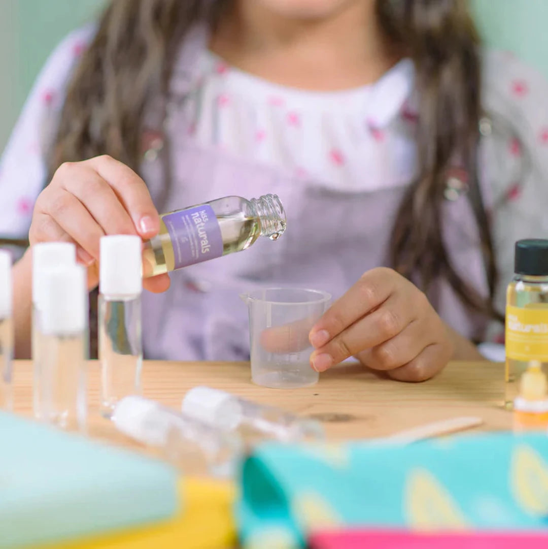 A cardboard box containing a Kiss Naturals Lava Lip Gloss Kit. The box is orange and white with the product name and a colorful illustration of a dragon. It states that the kit is 100% natural, made in Canada, and suitable for ages 6 and up.