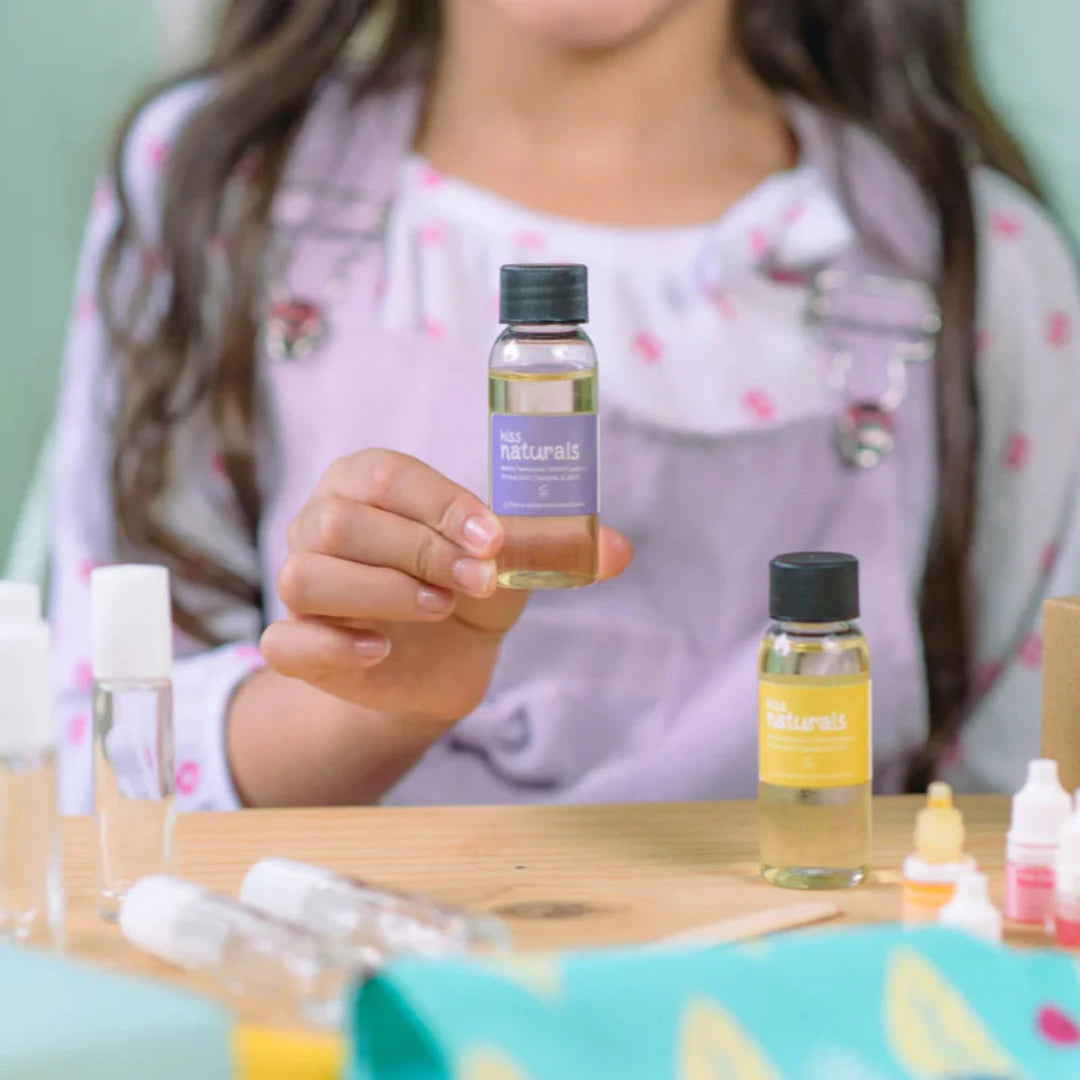 A cardboard box containing a Kiss Naturals Lava Lip Gloss Kit. The box is orange and white with the product name and a colorful illustration of a dragon. It states that the kit is 100% natural, made in Canada, and suitable for ages 6 and up.