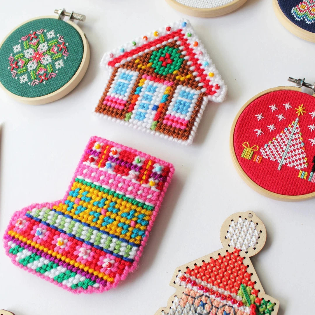 A collection of colorful Christmas ornaments made using plastic canvas. The ornaments include a gingerbread house, a Christmas stocking, Santa Claus, a snowman, a Christmas tree, and various ornaments.