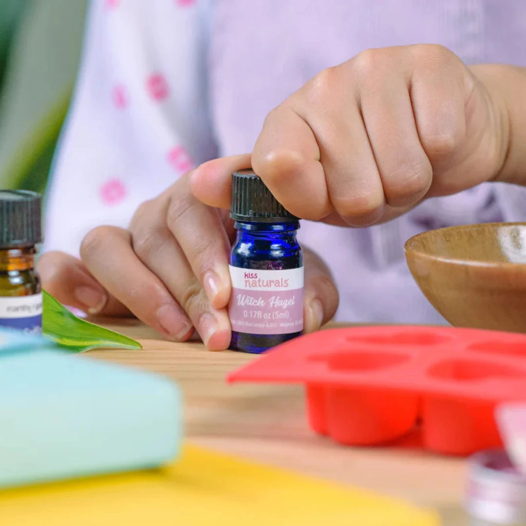 A cardboard box containing a Kiss Naturals Bath Bomb Kit. The box is green and white with the product name and a colorful illustration of bath bombs. It states that the kit is 100% natural, made in Canada, and suitable for ages 6 and up.
