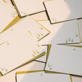 Set of greeting cards with gold edges and small green floral illustrations on a light background