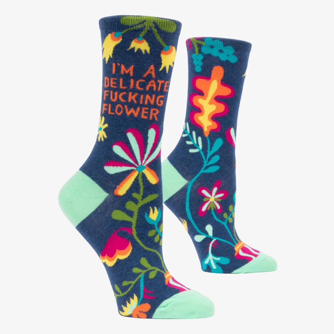 A pair of dark blue women's crew socks with a vibrant, abstract floral pattern in shades of orange, yellow, pink, fuchsia, green, and light blue. Text on one sock reads "I'M A DELICATE FUCKING FLOWER".