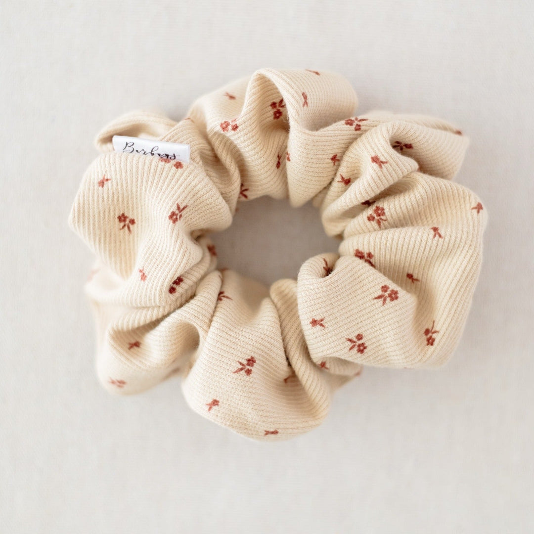 Beige scrunchie with small red floral patterns on a light gray background