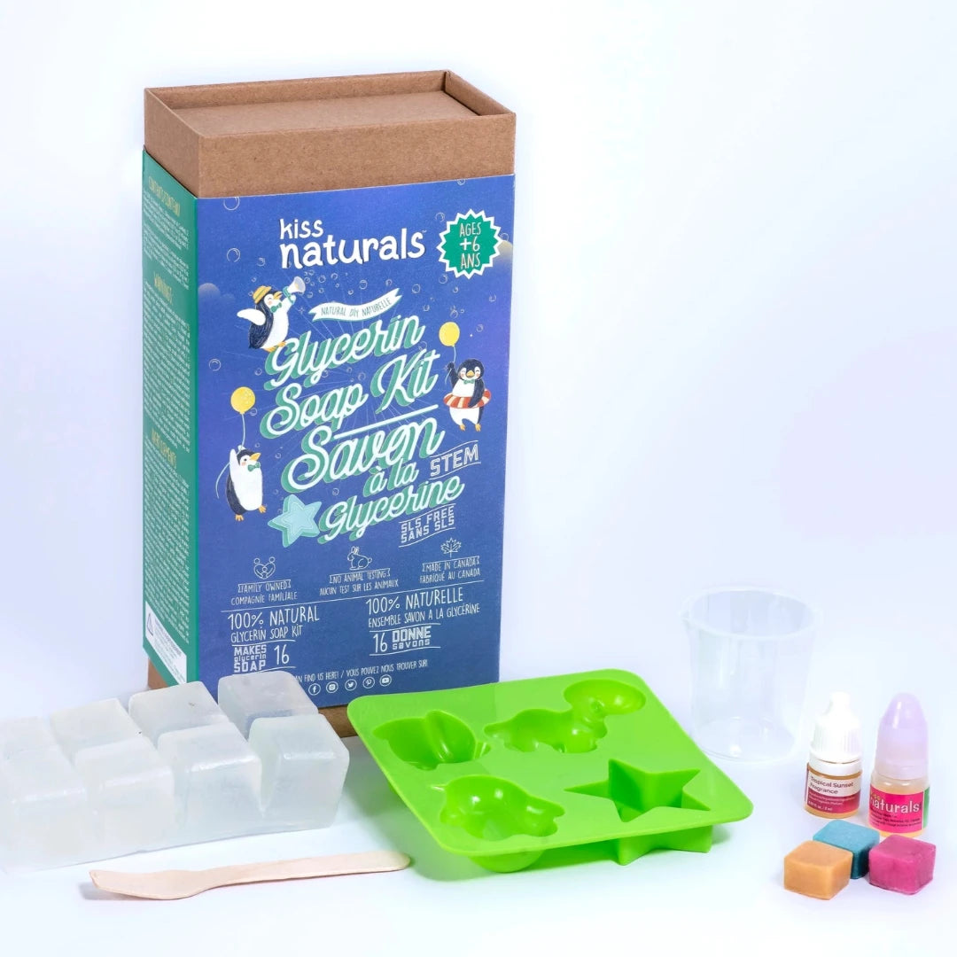 A cardboard box containing a Kiss Naturals Glycerin Soap Kit. The box is blue and white with the product name and a colorful illustration of penguins. It states that the kit is 100% natural, made in Canada, and suitable for ages 6 and up.