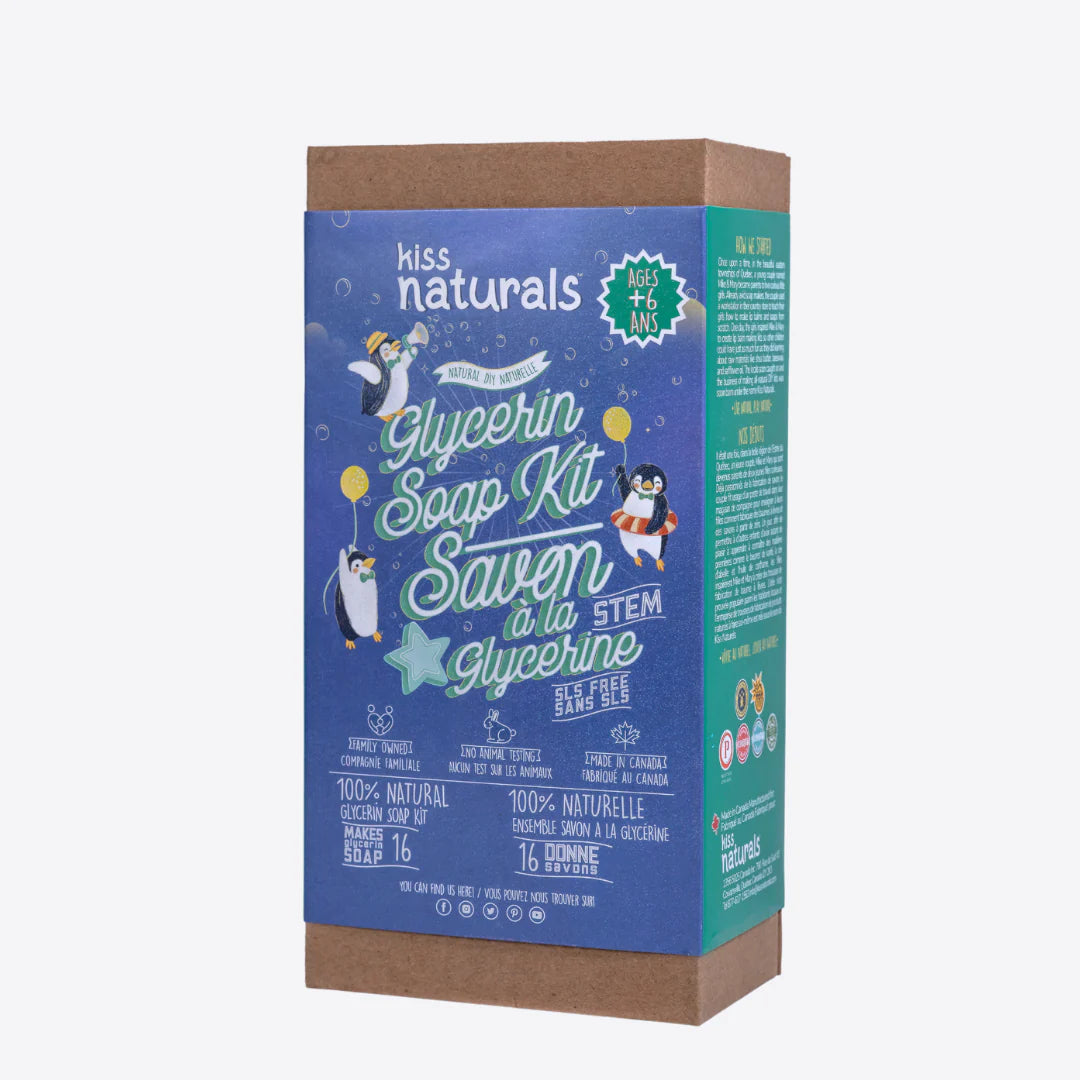 A cardboard box containing a Kiss Naturals Glycerin Soap Kit. The box is blue and white with the product name and a colorful illustration of penguins. It states that the kit is 100% natural, made in Canada, and suitable for ages 6 and up.