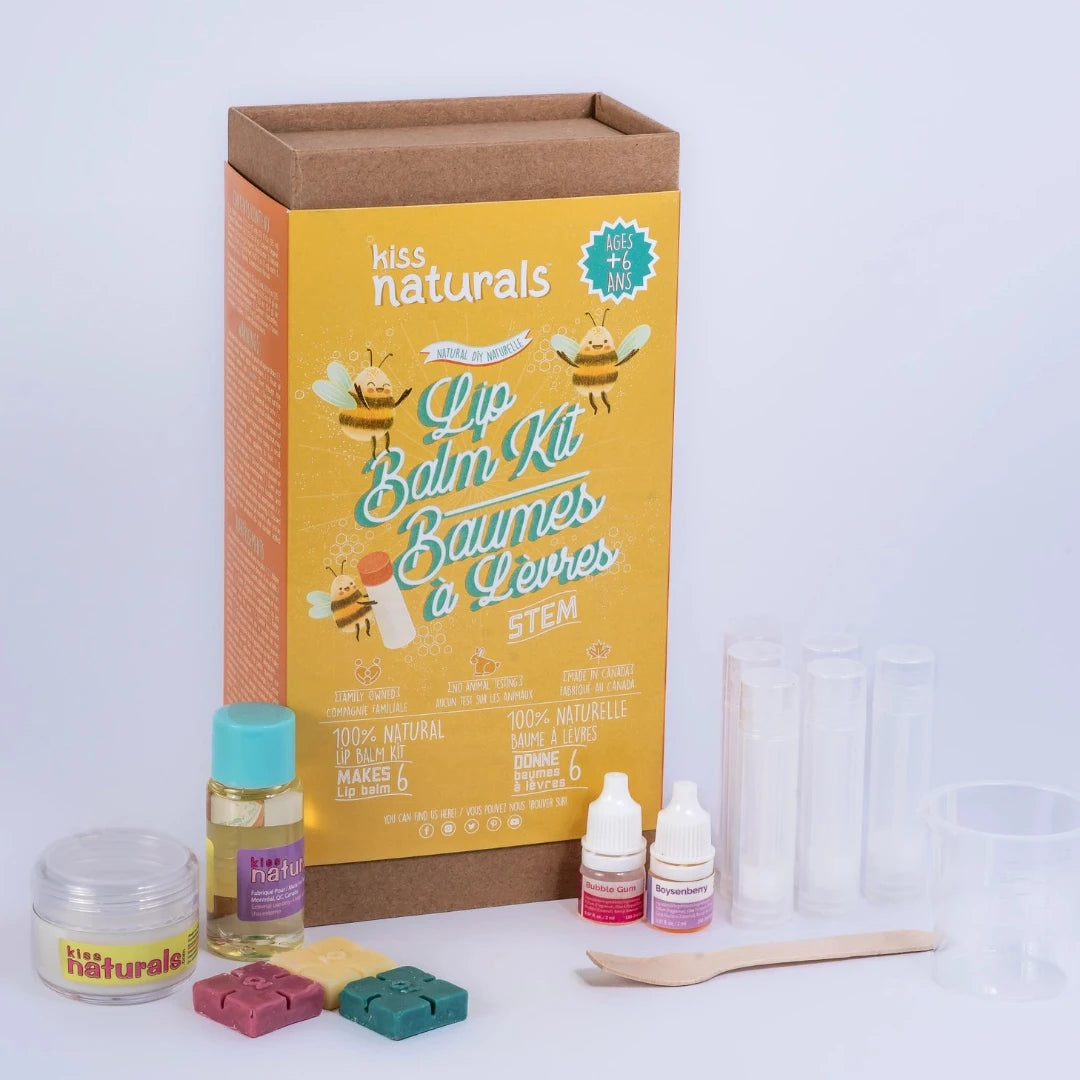 A cardboard box containing a Kiss Naturals Lip Balm Kit. The box is yellow and white with the product name and a colorful illustration of bees. It states that the kit is 100% natural, made in Canada, and suitable for ages 6 and up.