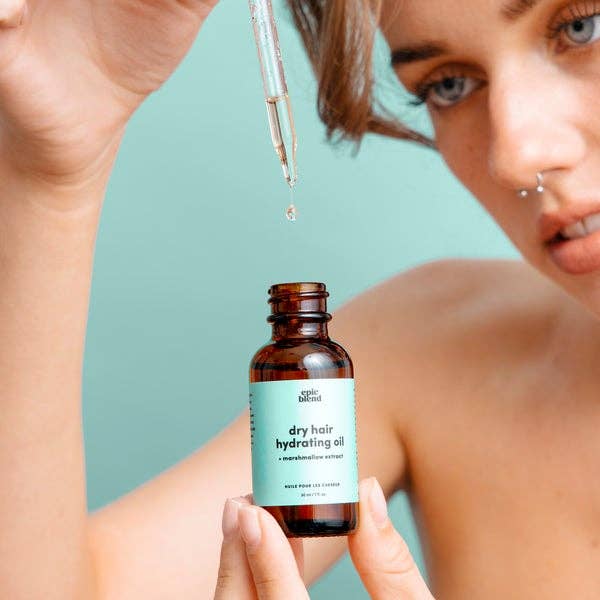 A small, amber glass dropper bottle of Epic Blend dry hair hydrating oil, featuring a light blue label with product details.
