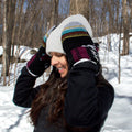 Person wearing a colorful beanie and gloves in a snowy forest