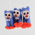 A felt ornament of a cat in a blue snow suit skiing down a hill on red skies. The cat has a white face.