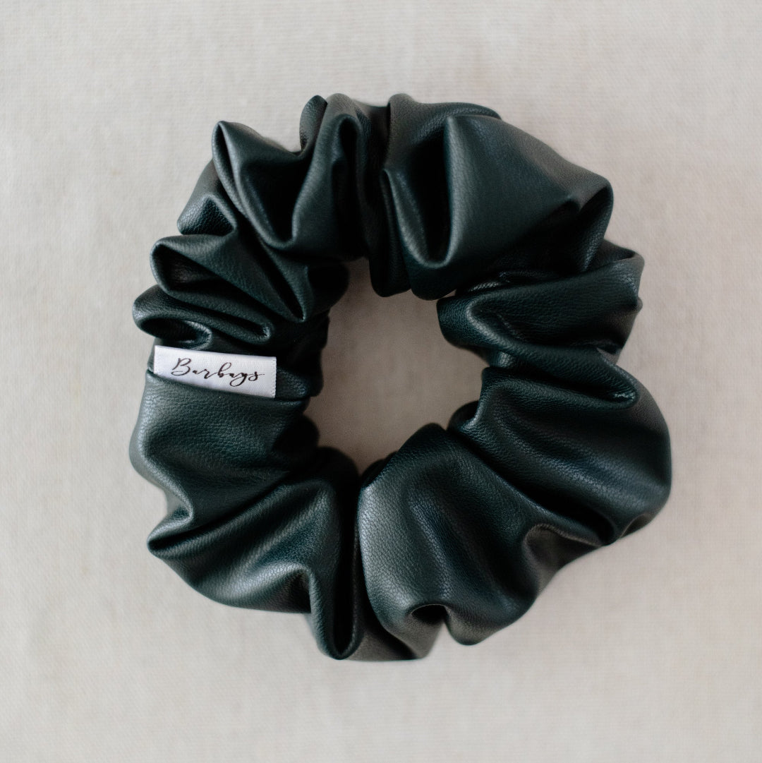 Dark green scrunchie with a brand label on a light gray background